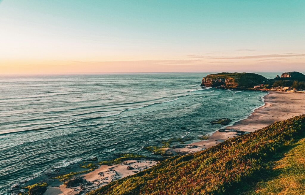 Imagem da beira da praia de Torres, com o Parque da Guarita ao fundo.